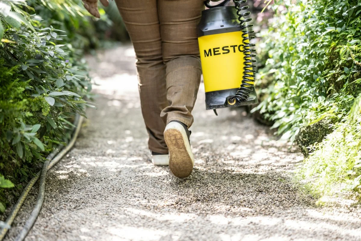 Pest control technician carrying a sprayer tank in Tucson, Arizona